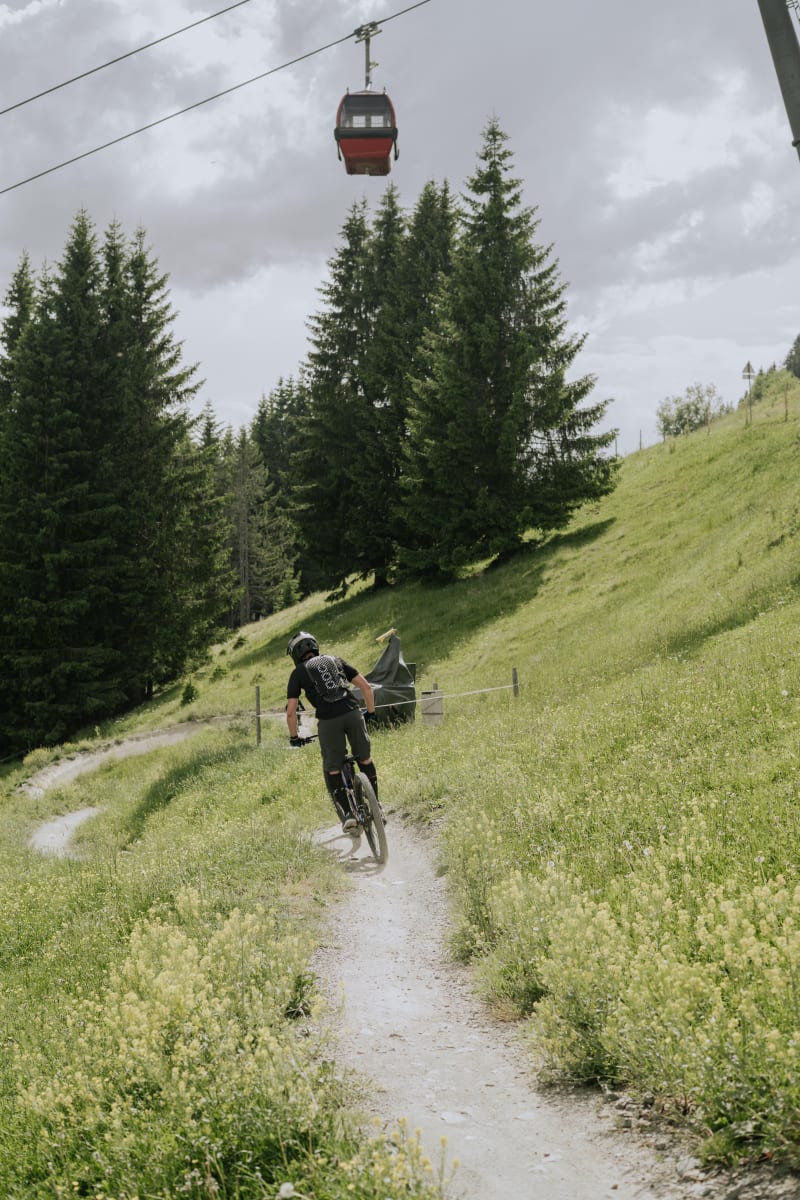 Ein Radfahrer auf einem Trails durch das Glemmtal, mit einer Seilbahn, die über die Bäume schwebt.