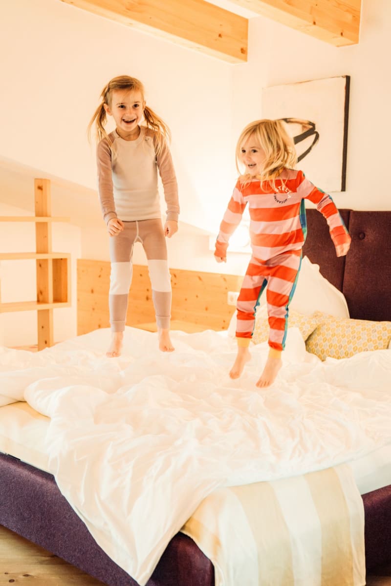 Zwei Kinder springen fröhlich auf einem Bett im Glemmtalerhof in Hinterglemm.