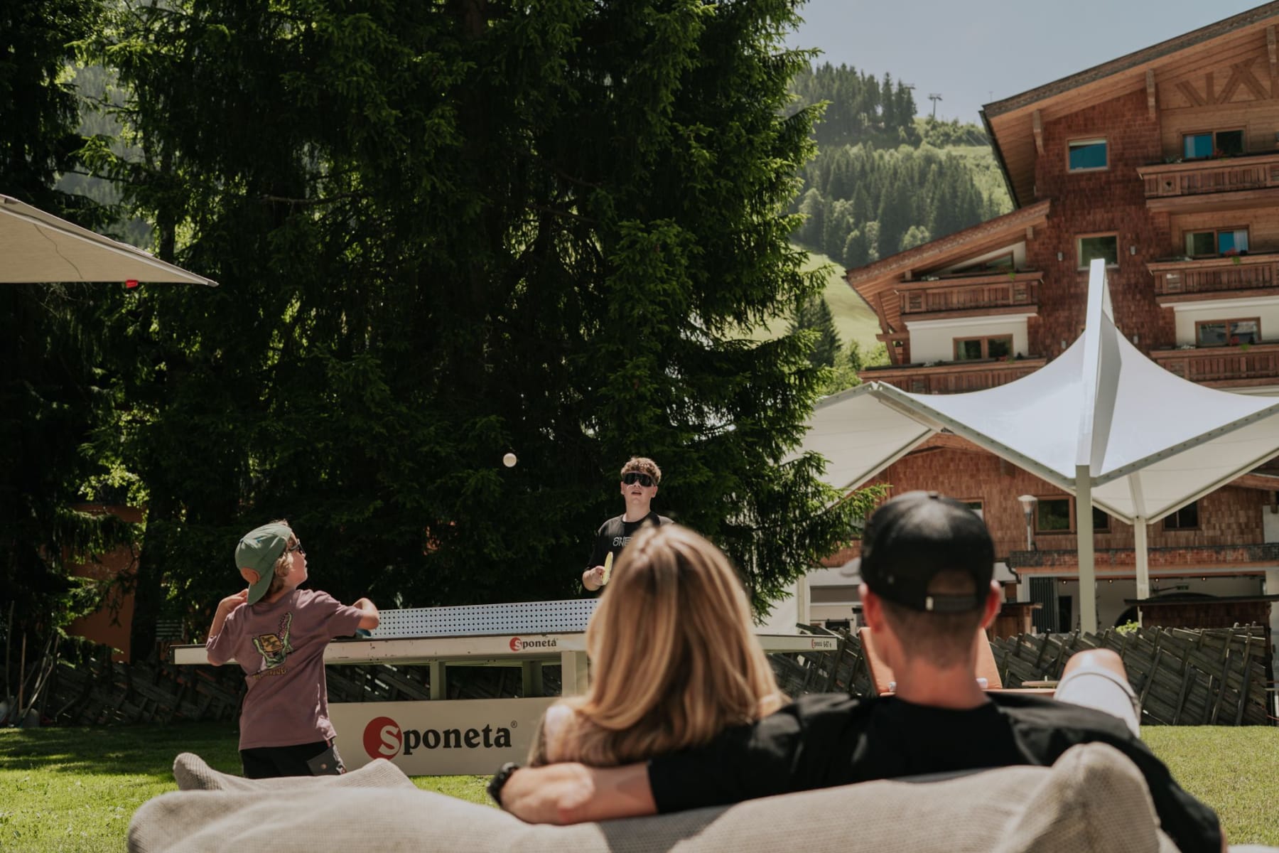 Im Glemmtal spielt ein Kind Tischtennis, während Erwachsene entspannt auf einer Couch sitzen.