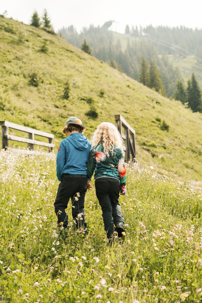Kinder spazieren im Glemmtal über eine blühende Wiese.