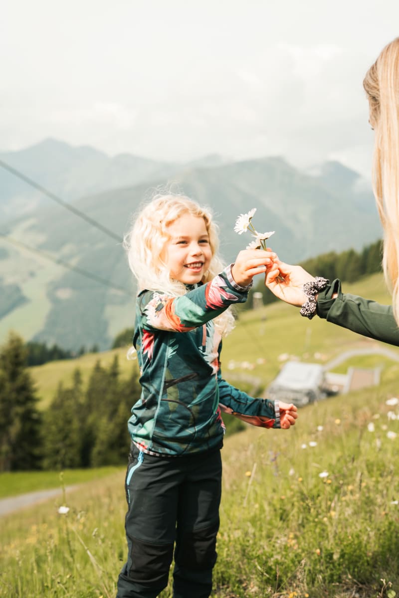 Ein Kind reicht einer anderen Person eine Blume im malerischen Glemmtal in Hinterglemm.
