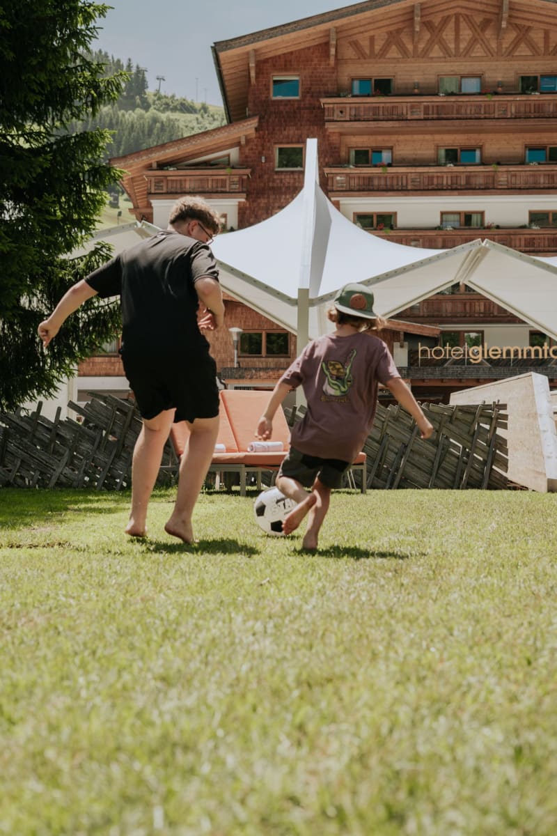 Ein Erwachsener und ein Kind spielen im Glemmtal im Garten mit einem Fußball.