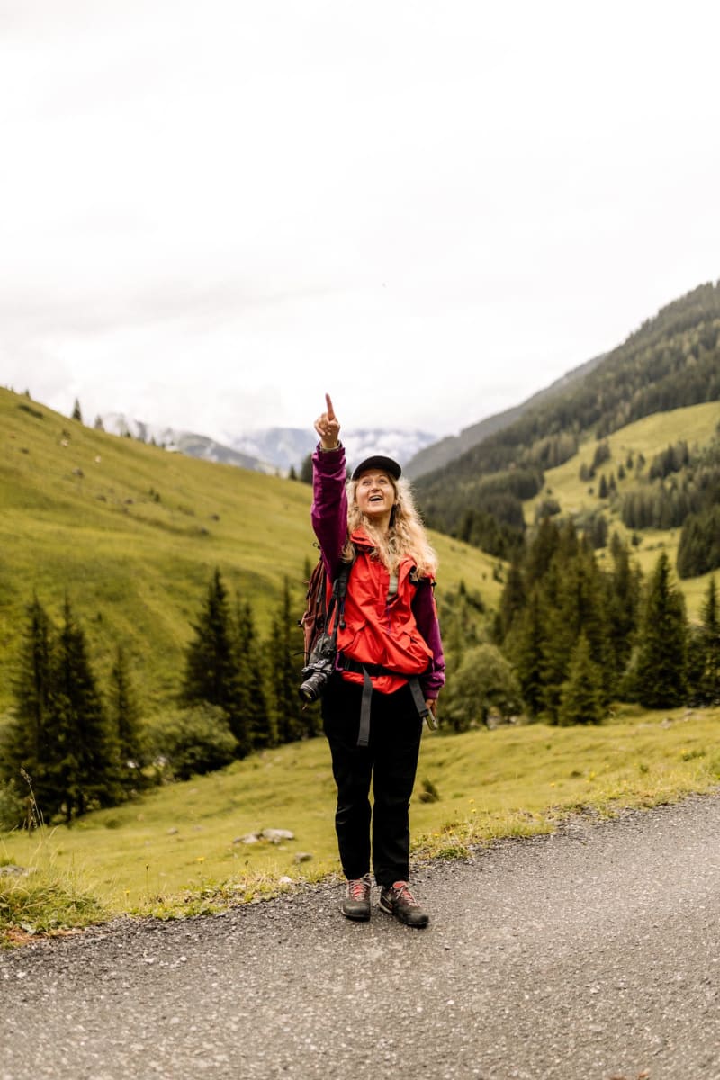 Eine Frau zeigt nach oben im Glemmtal, während sie in der Natur wandert.