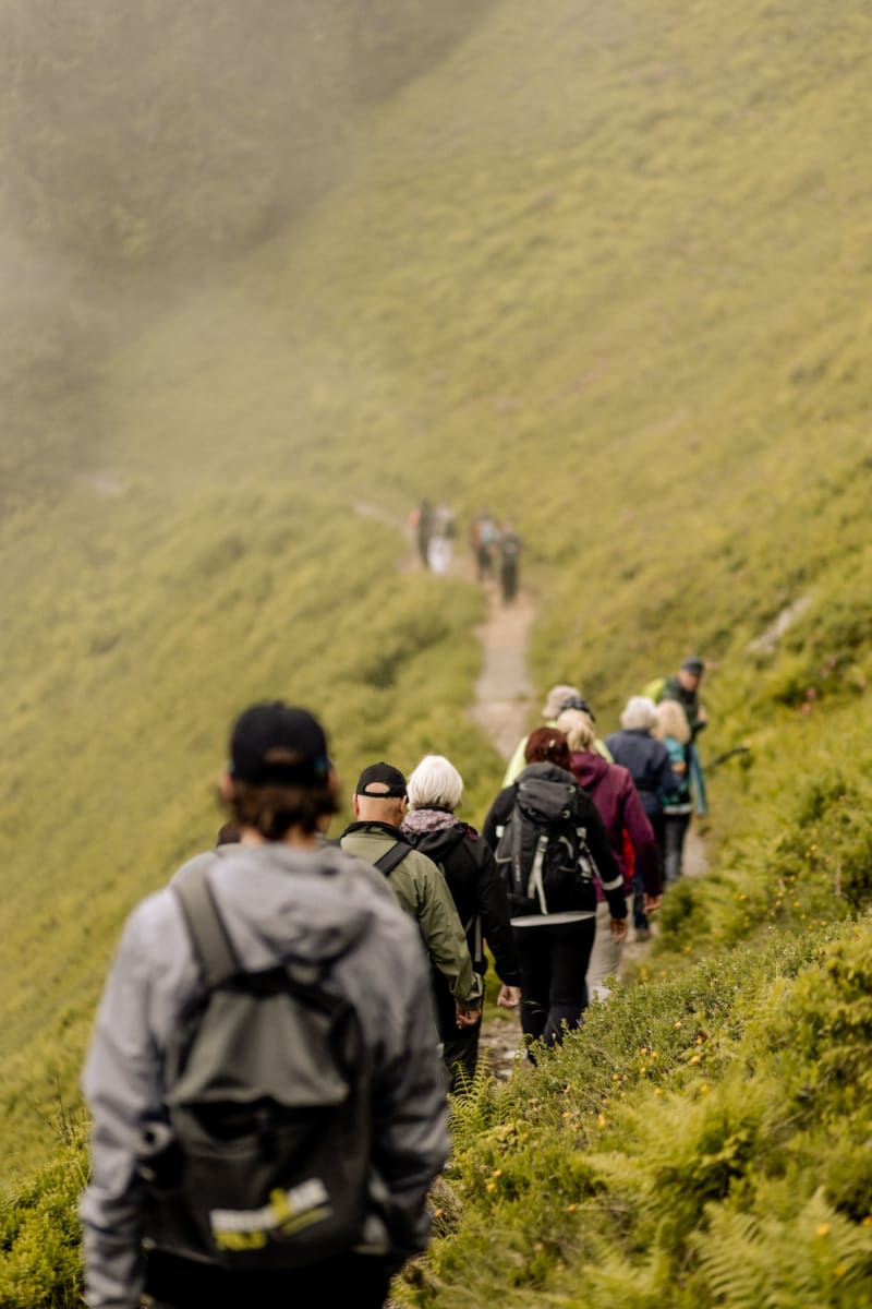 Wanderer gehen den Pfad im Glemmtal entlang, umgeben von grünen Hügeln.