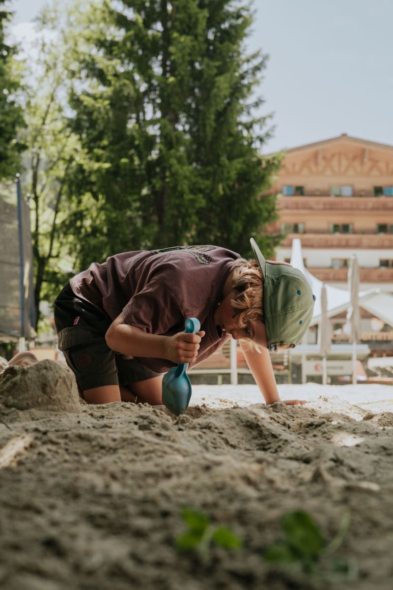 Ein Junge spielt im Sand vor dem Glemmtalerhof in Hinterglemm