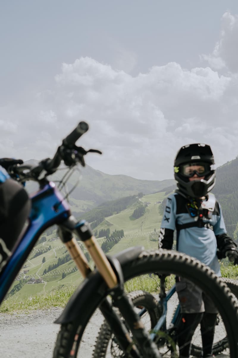 Kleiner Junge in Schutzkleidung steht im Glemmtal mit Mountainbike.