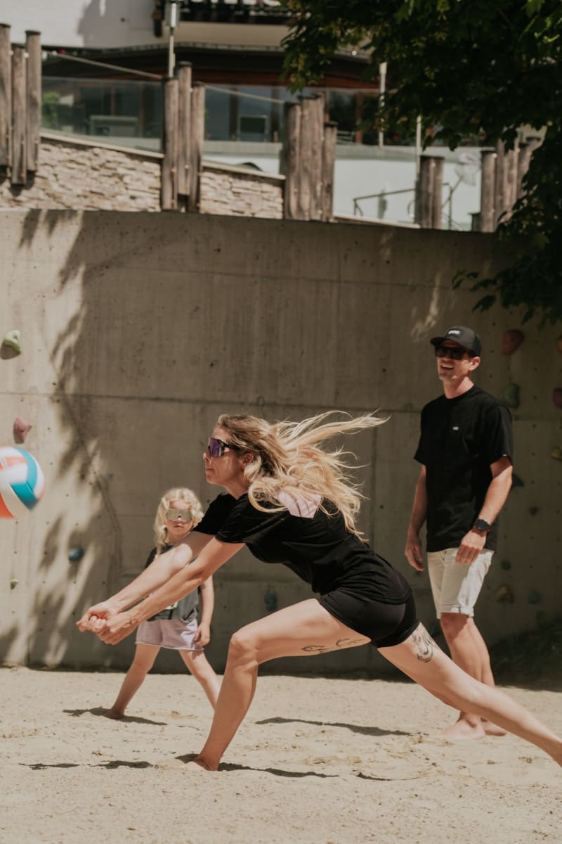 Eine Frau spielt Volleyball am Glemmtalerhof in Hinterglemm mit einem Kind und einem Mann.