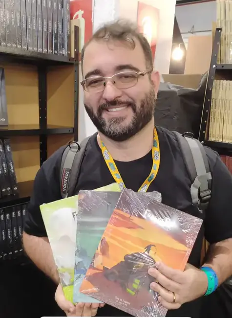 Rafael Mendes segurando livros do RPG Fragged Empire durante evento de RPG.