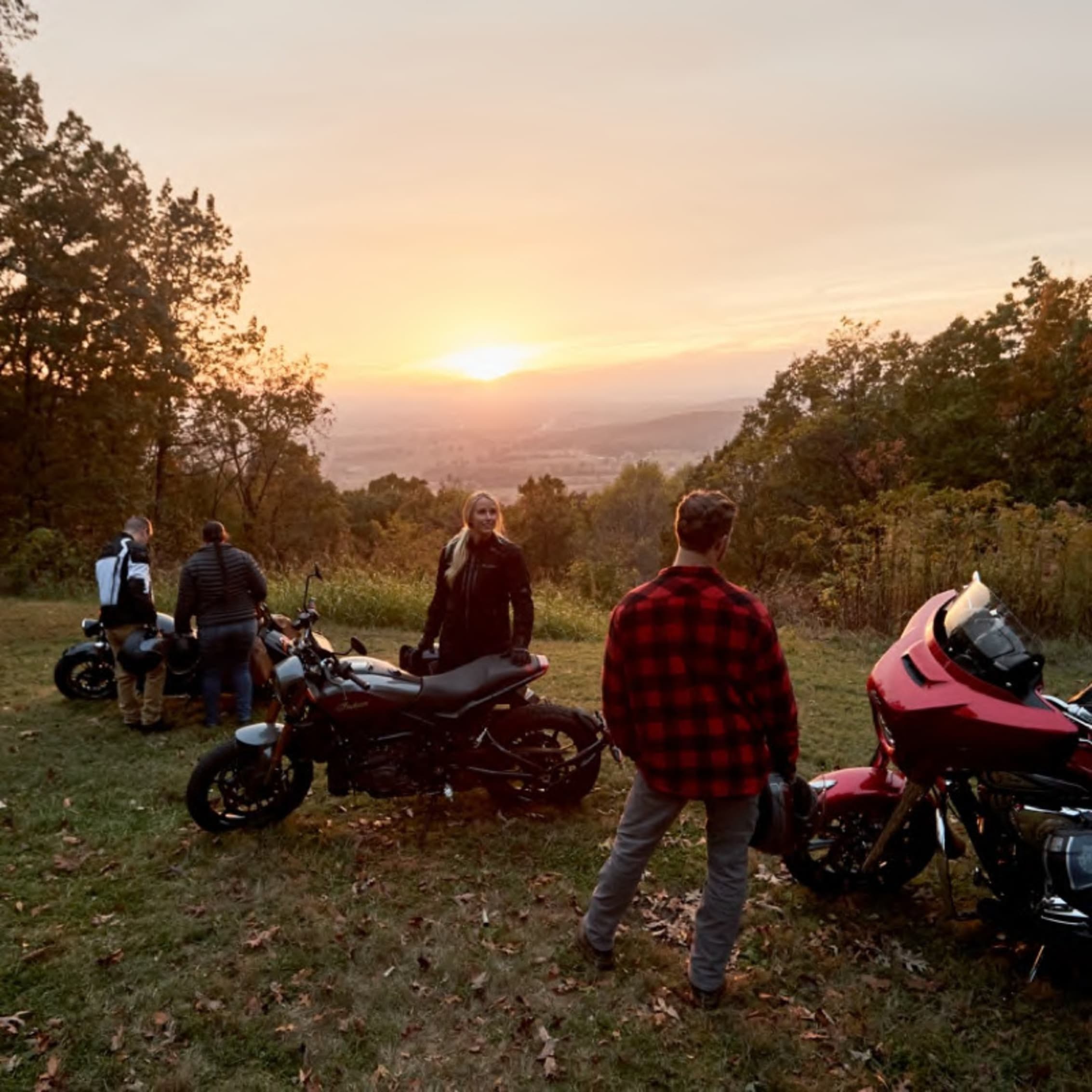 Group of friends with motorcycles enjoying a beautiful sunset view from a hill, capturing the spirit of adventure and freedom on the open road