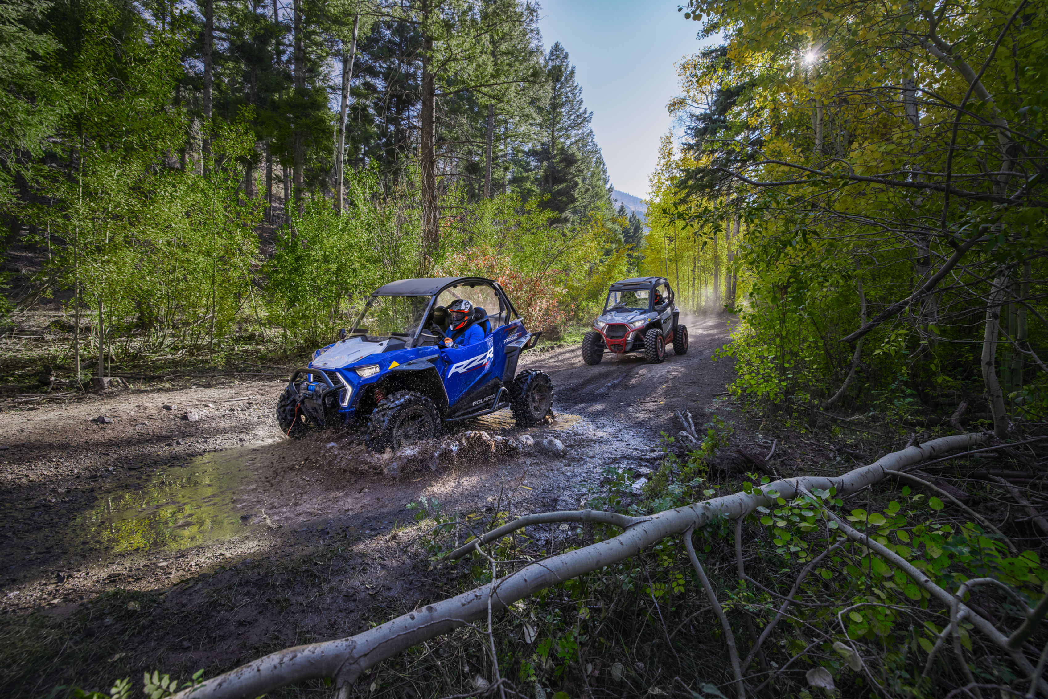 Two Polaris RZRs on muddy trail