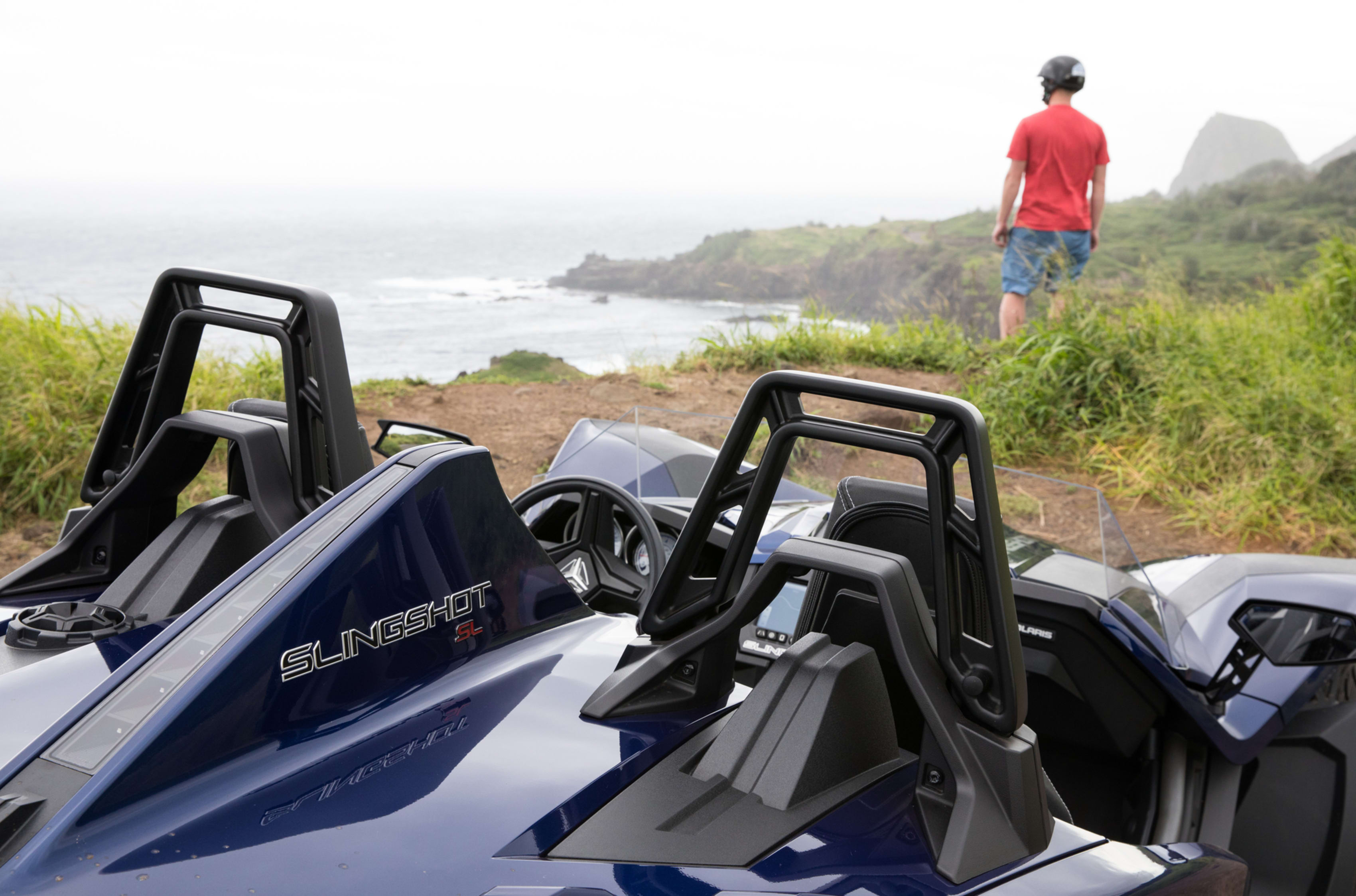 Man standing near Polaris Slingshot on Hawaiian coastline