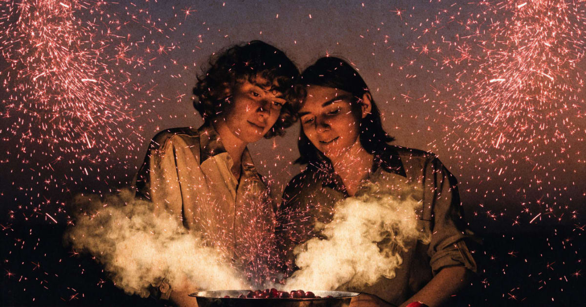 A couple stands at a stove where popping cranberries burst upward like tiny garnet-red fireworks against the evening light.