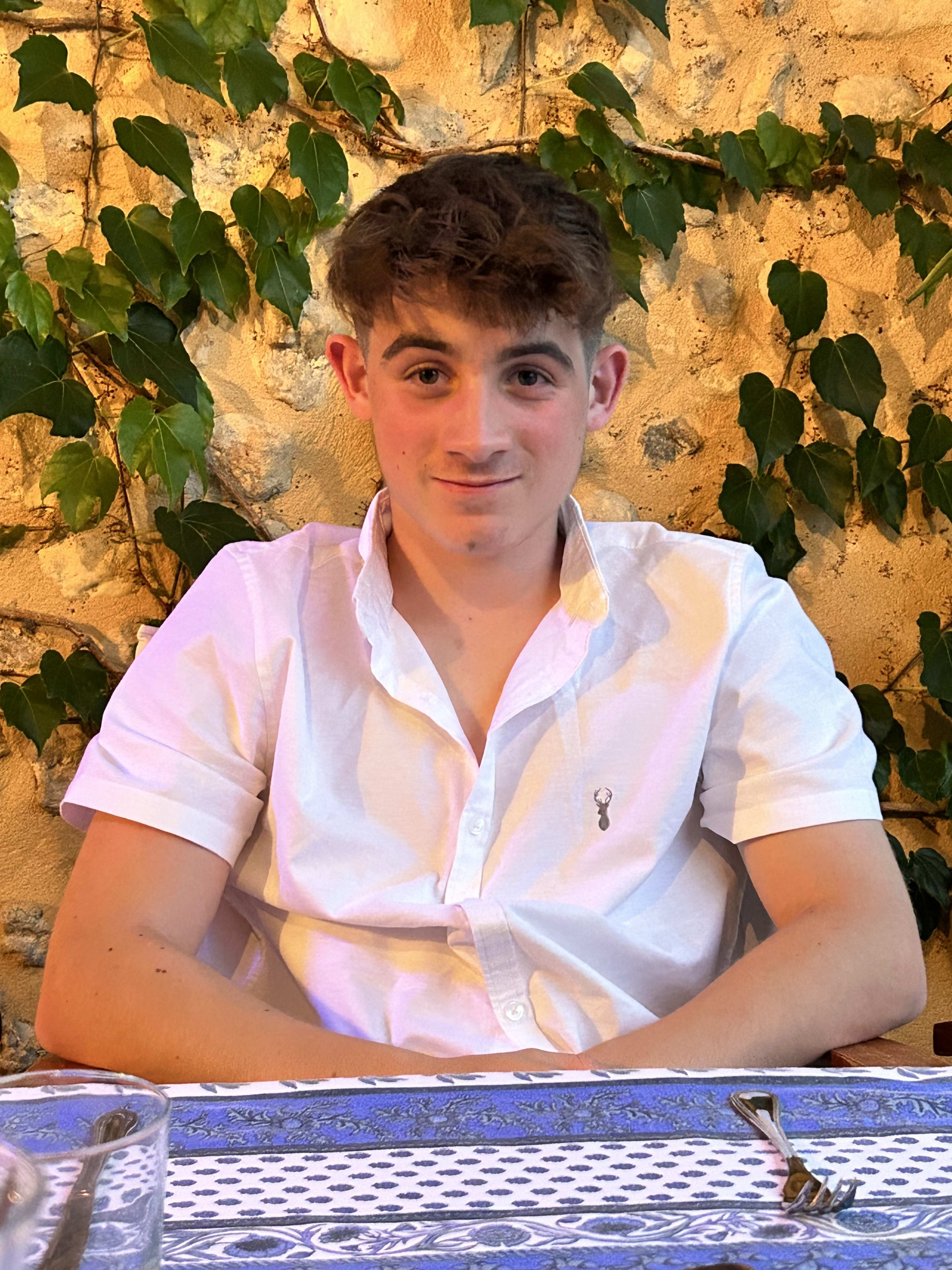 Charlie at a Mediterranean restaurant, white shirt, brown curly hair, warm golden stone wall