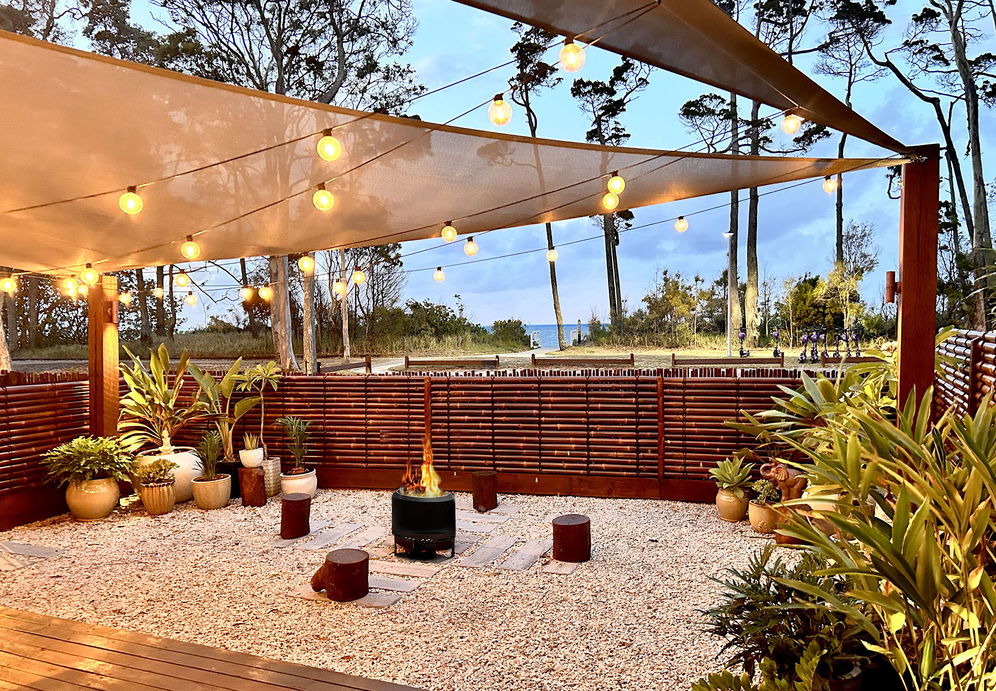 Outdoor garden with firepit and deck seating among tropical plants at Vila Paus Satu, with ocean views