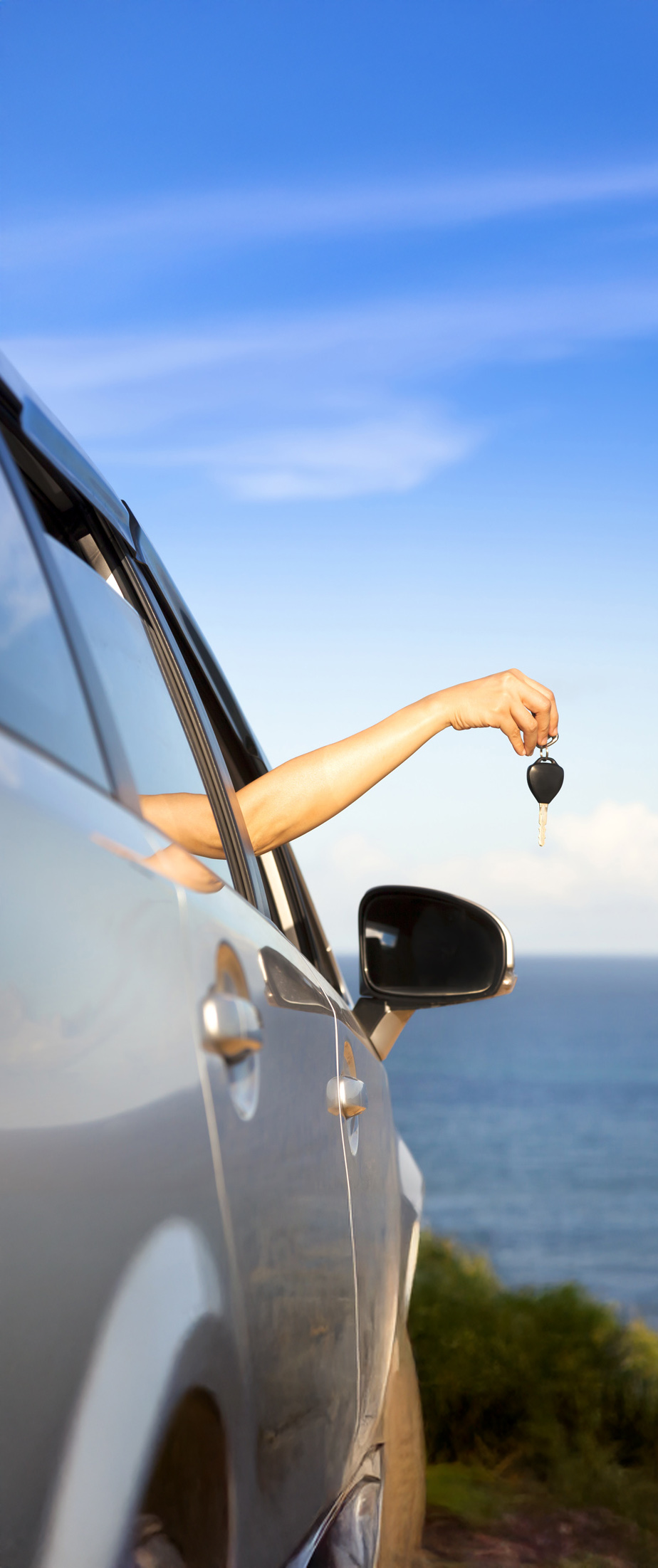 Hand holding car keys out a car window with the ocean in the background