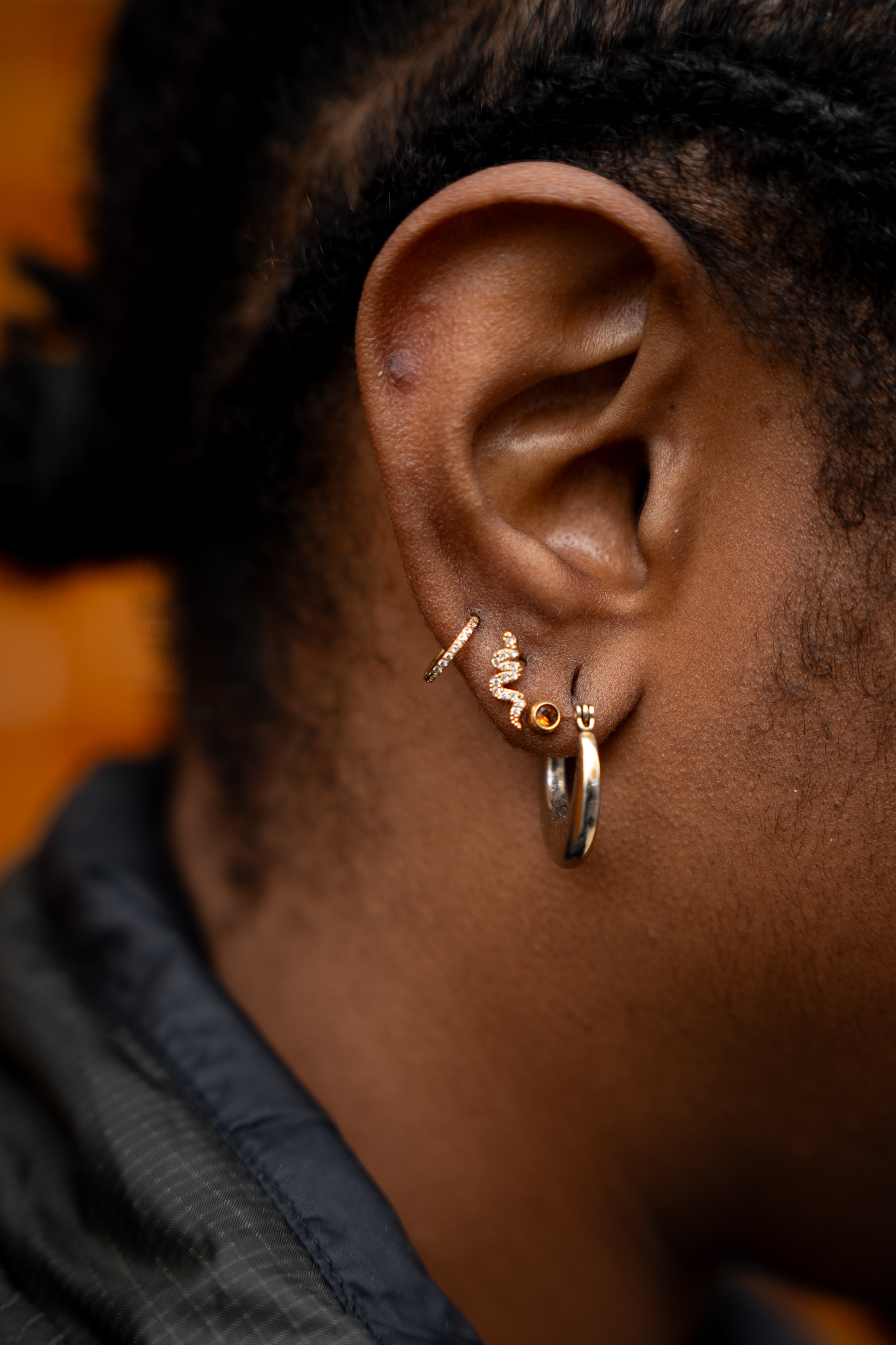 A close up of Esther's ear, she's wearing a hoop in her earlobe followed by three studs and a very small hoop.