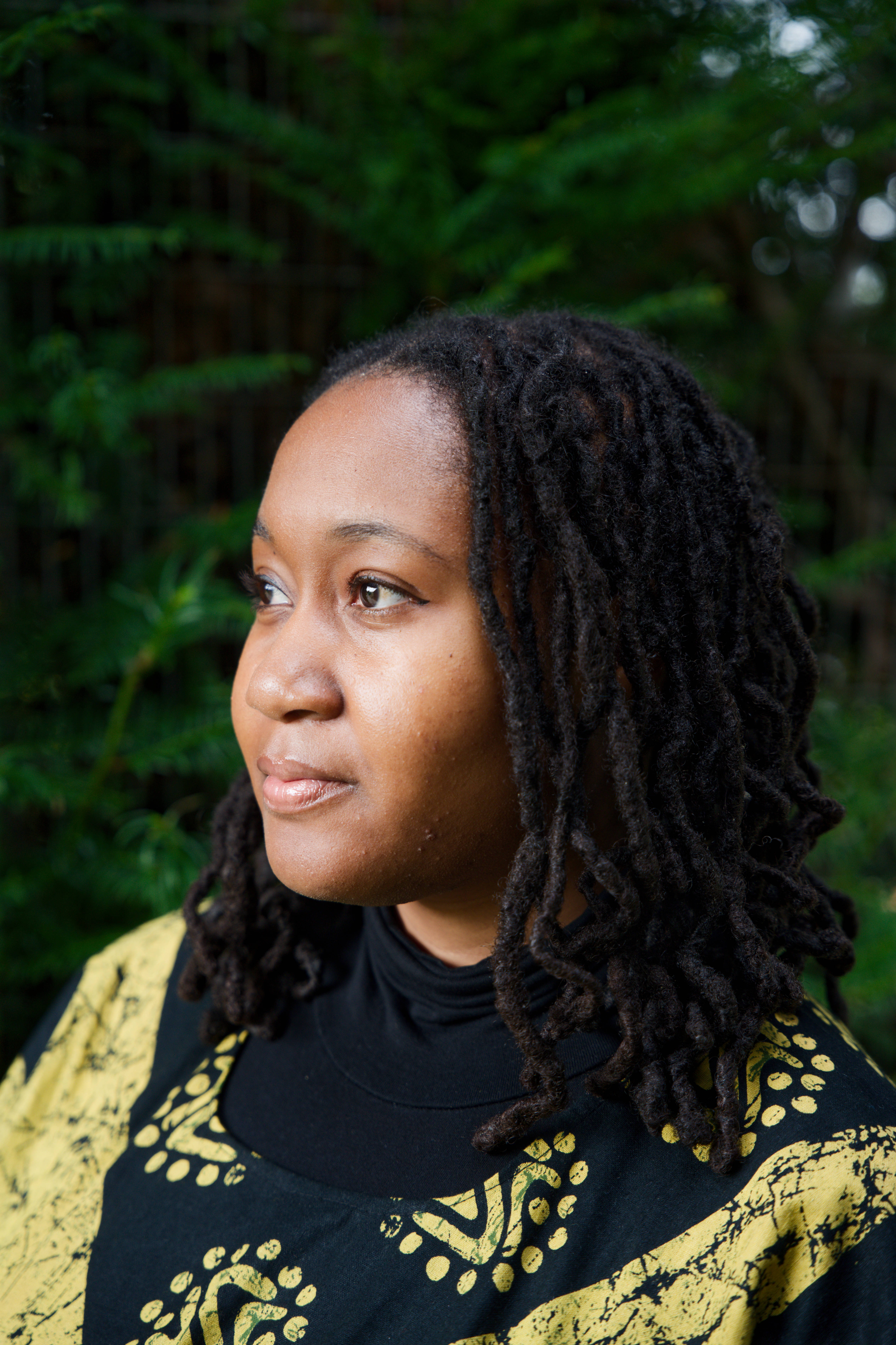 A picture of author Jackson P. Brown's profile. She's standing in front of a dark green hedge which is blurred.