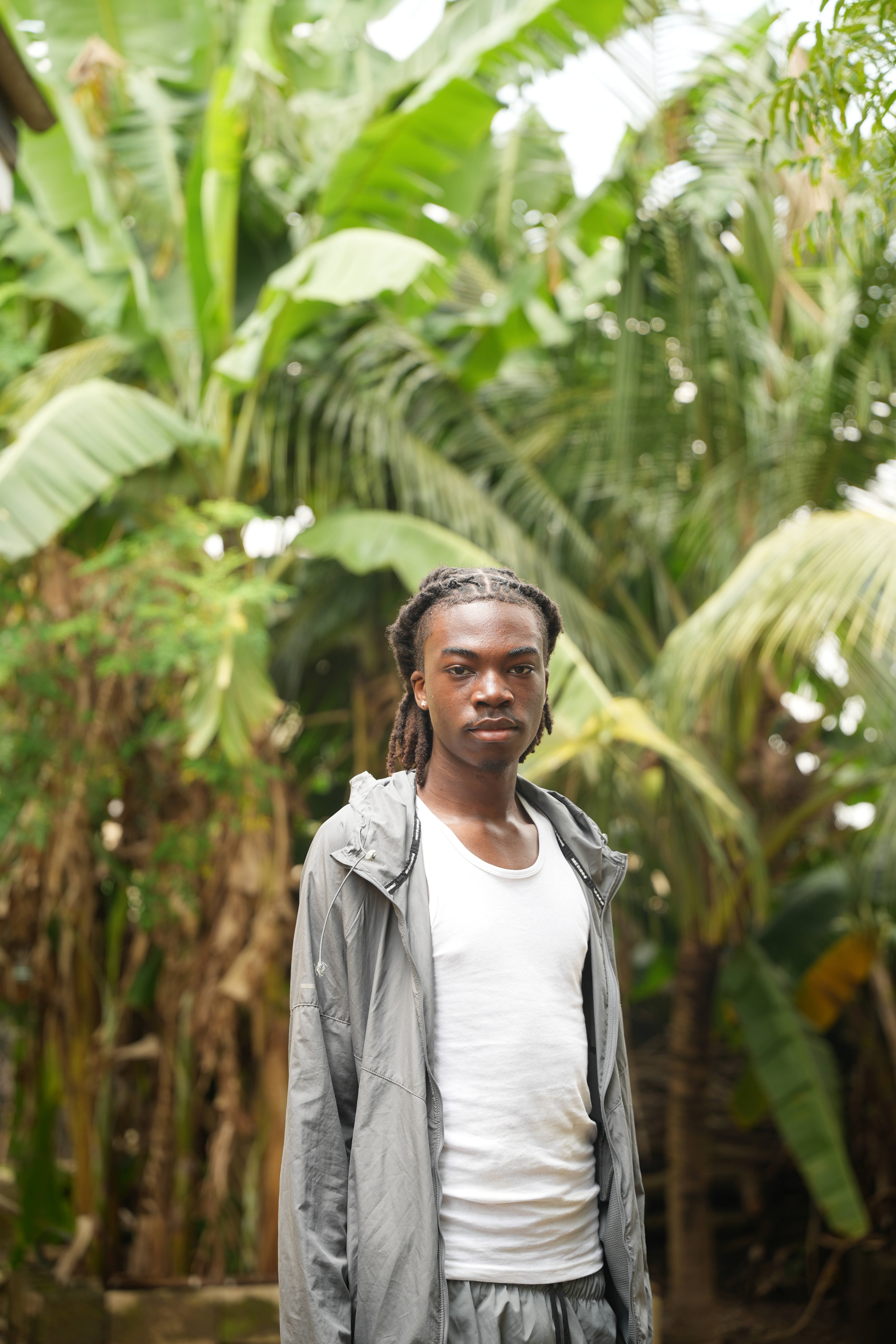 A full body portrait of Shubomi in Nigeria, there are palm trees behind him and they are slightly blurred
