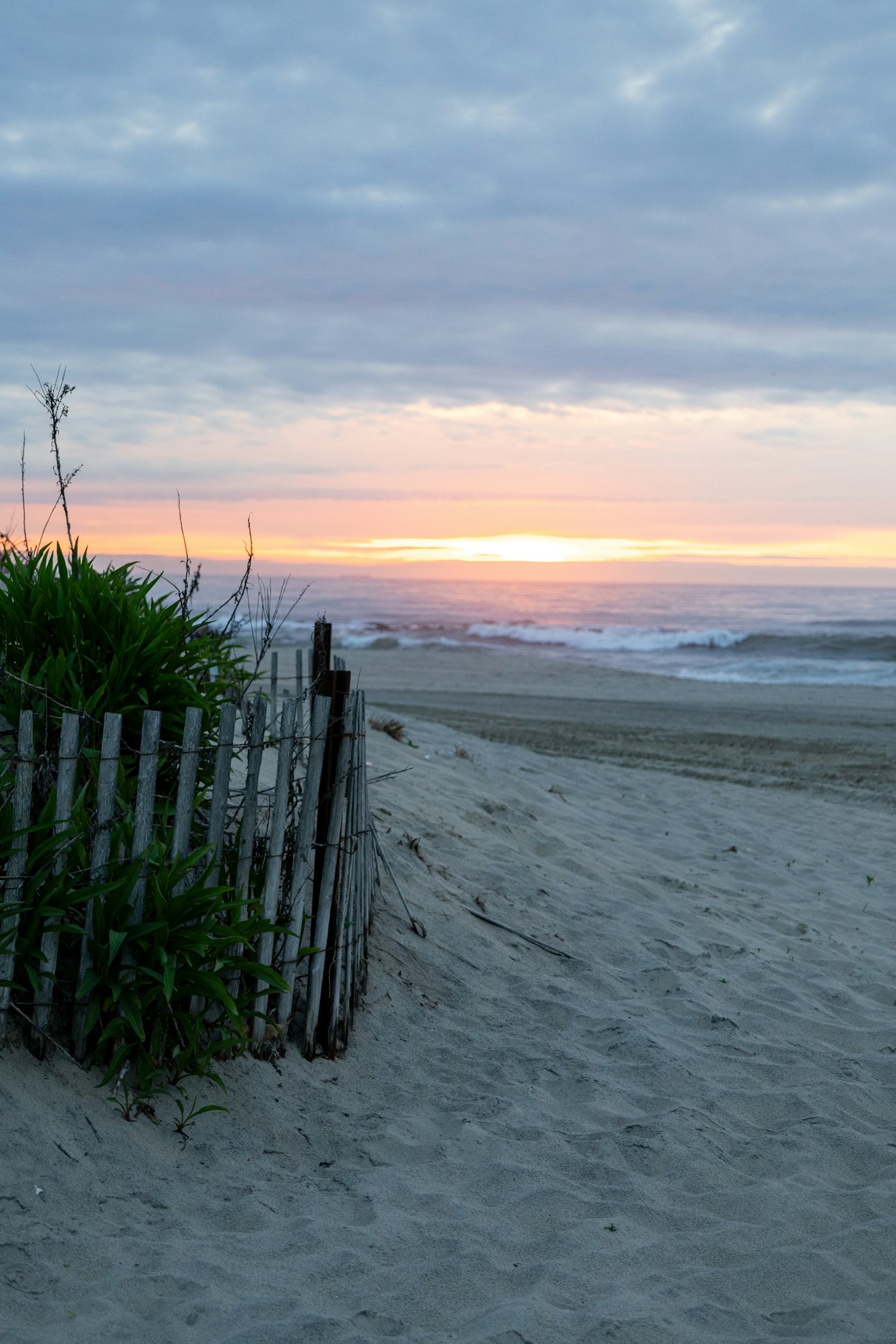 a fence on a beach with a sunset in the background