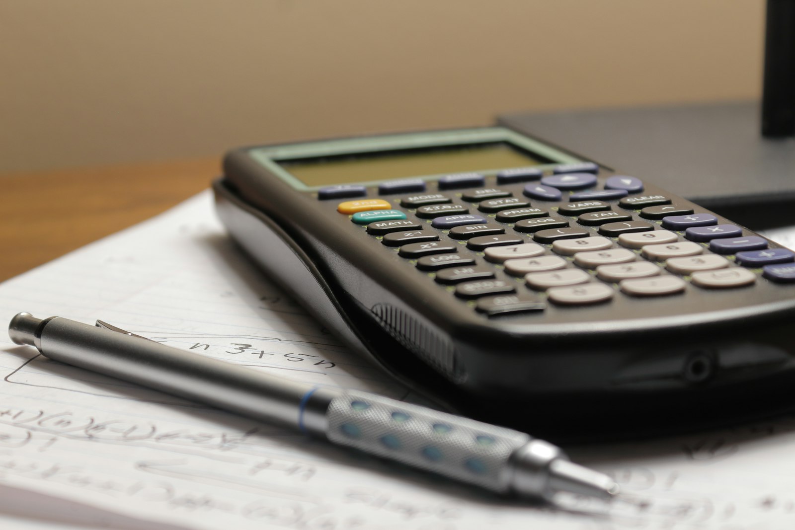 A calculator and a pen resting on a sheet of handwritten math