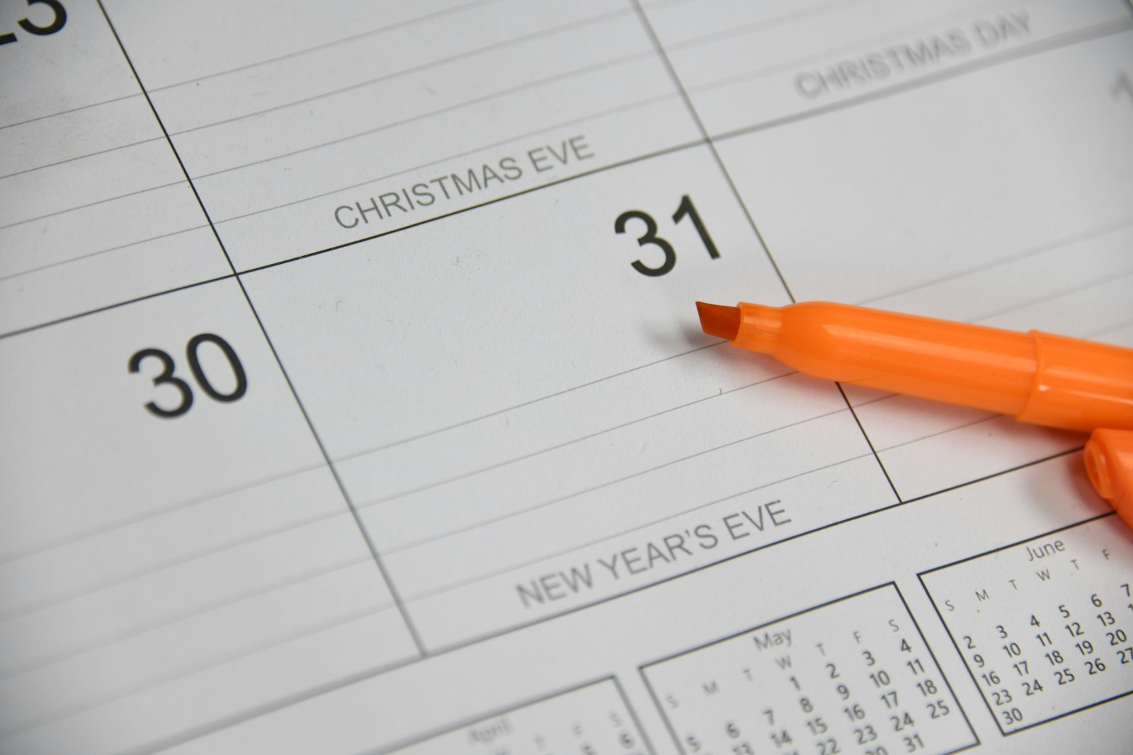 A hand marking a date on a paper wall calendar with a marker