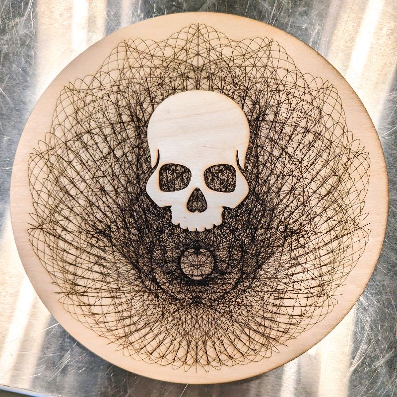 A wood cut circle with a complex SVG mandala cut into it, with a laser cut skull in the middle