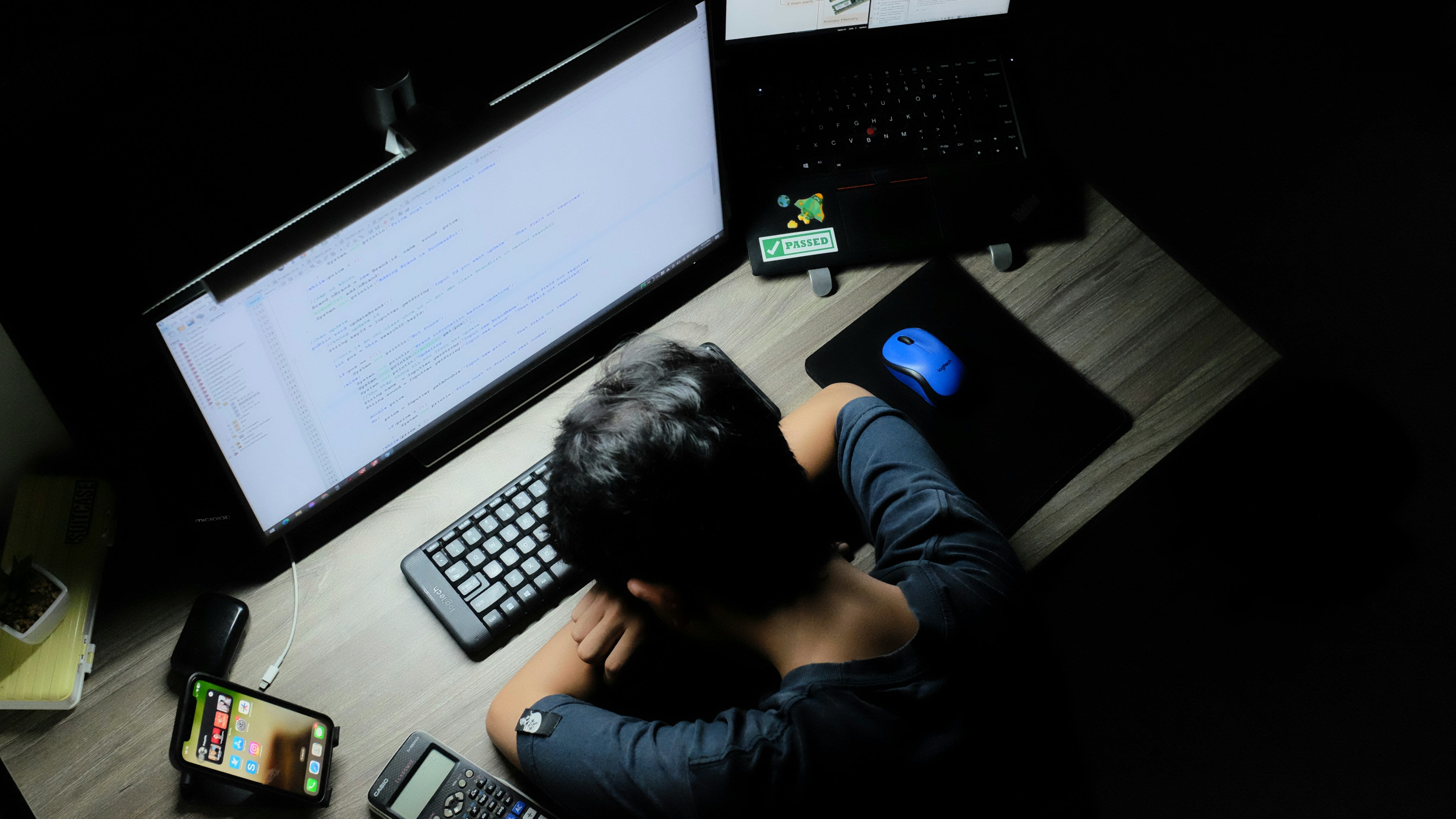 A stressed person taking off their glasses and rubbing their temples in front of a computer.