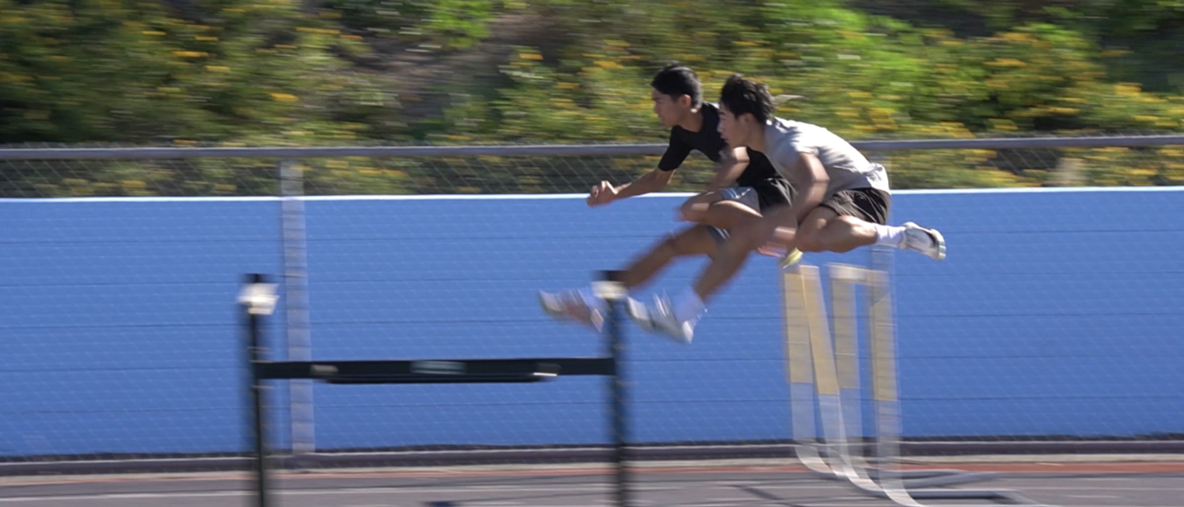Two hurdlers mid-air clearing a hurdle
