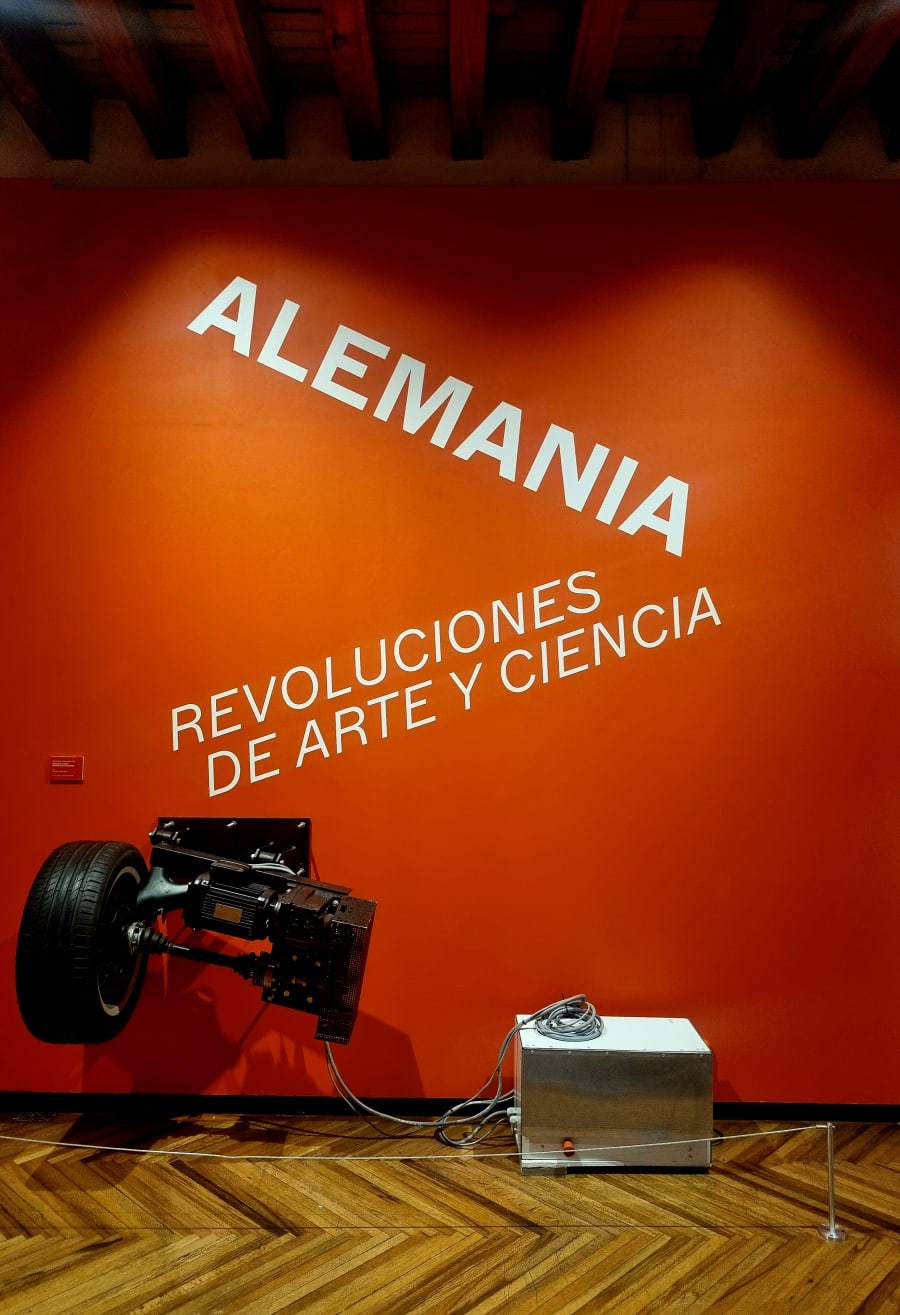 Muro de título naranja de la exposición Alemania, revoluciones de arte y ciencia, con una motocicleta en primer plano