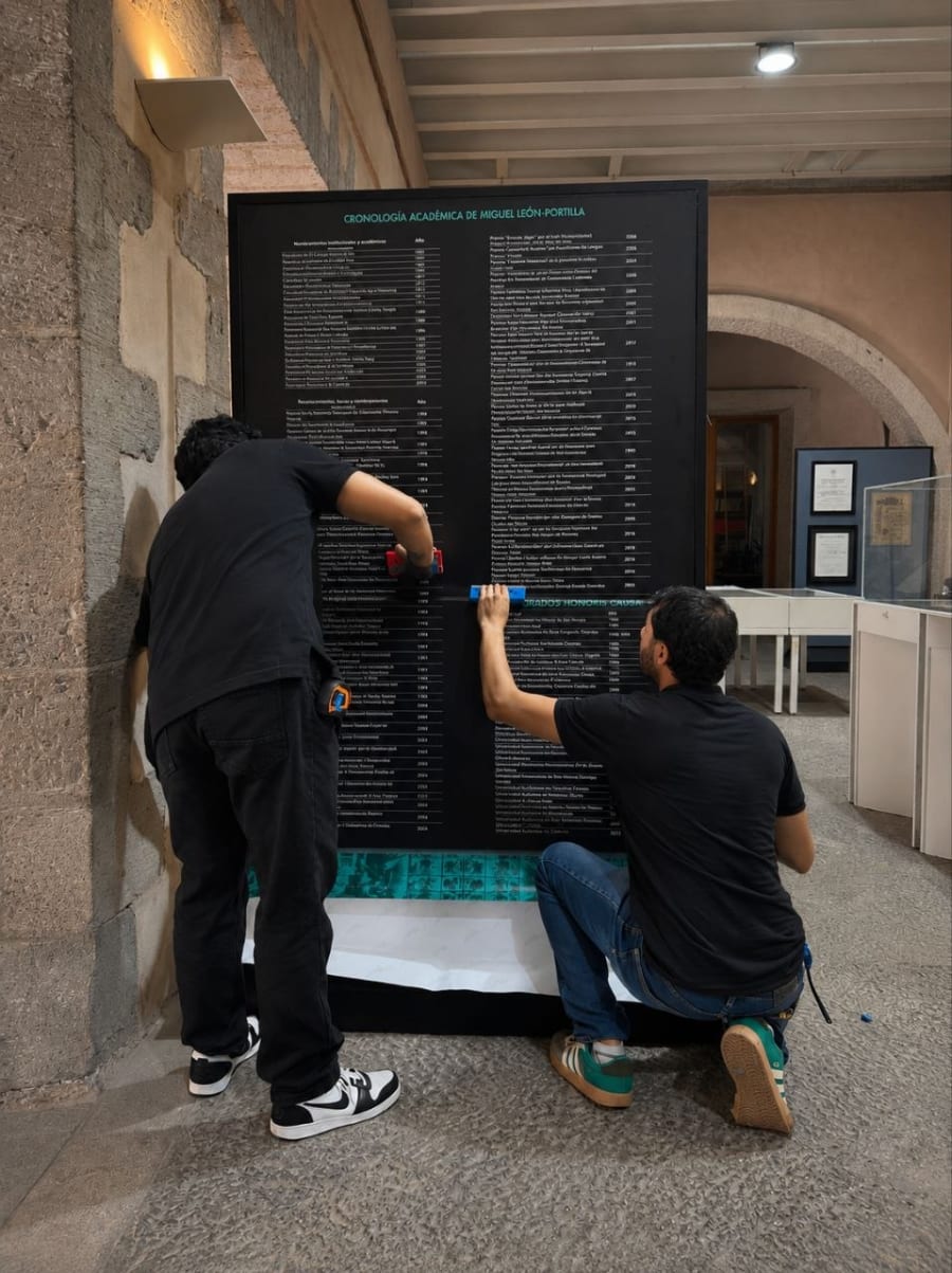 Dos personas instalando en sitio un panel expositivo oscuro con texto