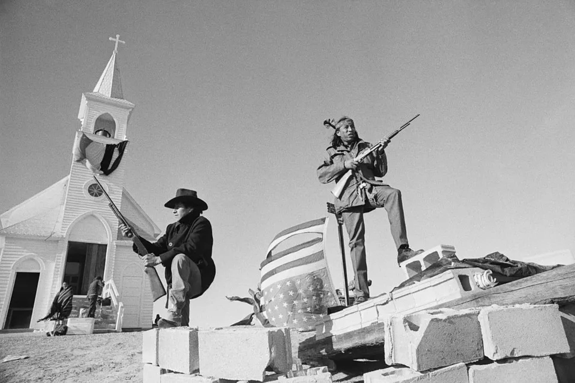 AIM members and an Oglala Lakota guard outside the Sacred Heart Catholic Church. AIM members and an Oglala Lakota guard outside the Sacred Heart Catholic Church.