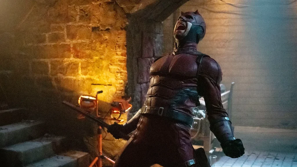 Daredevil (Charlie Cox) screaming passionately in his iconic red suit, standing in a dimly-lit, gritty underground setting.