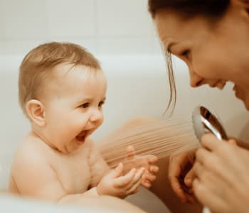 maman dans la baignoire avec son bébé, en train de jouer avec le pommeau de douche