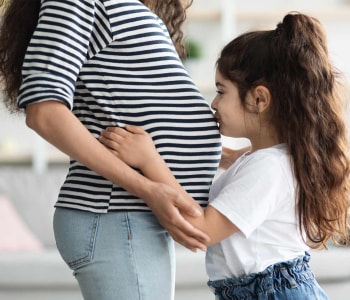 petite fille qui embrasse le ventre de sa maman enceinte