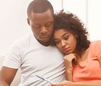 Couple enlacé sur un canapé qui semble déçu. La femme tient un test de grossesse dans sa main