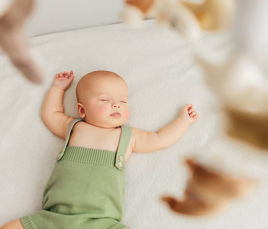 bébé en train de dormir dans son lit parapluie avec un mobile au-dessus de lui