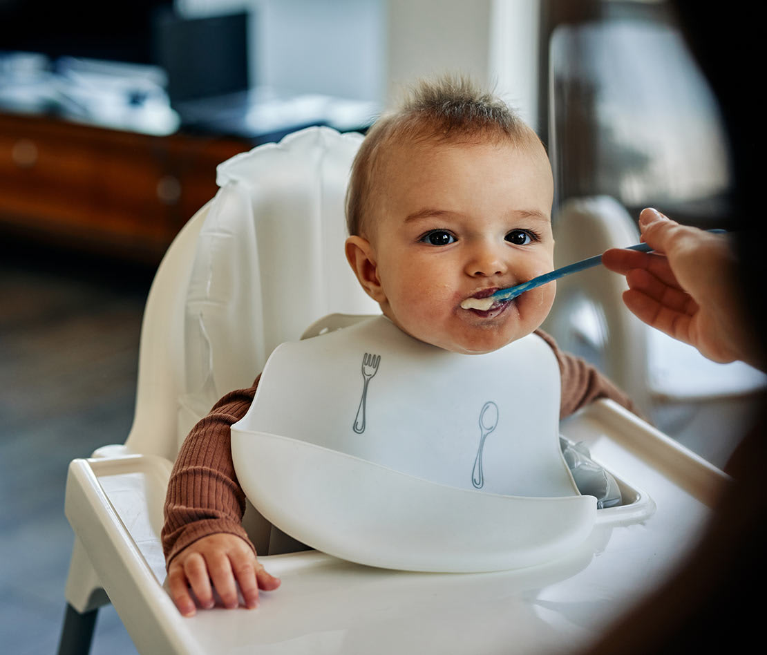 bébé en train de manger à la cuillère dans sa chaise haute avec son bavoir