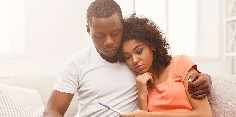 Couple enlacé sur un canapé qui semble déçu. La femme tient un test de grossesse dans sa main