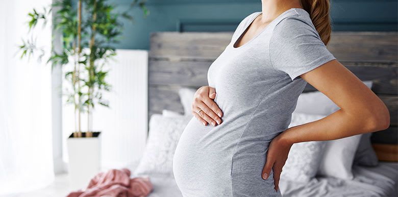 Jeune femme enceinte qui souffre de douleurs lombaires et pose une main sur son ventre
