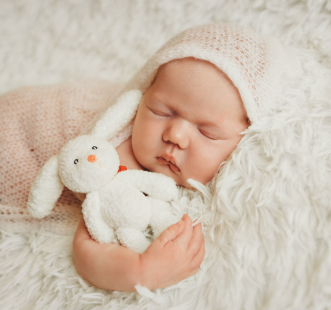 bébé dort avec un bonnet en laine blanc et un doudou en forme de lapin blanc