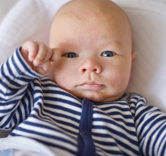 bébé yeux bleu en pyjama blanc et bleu allongé dans son lit