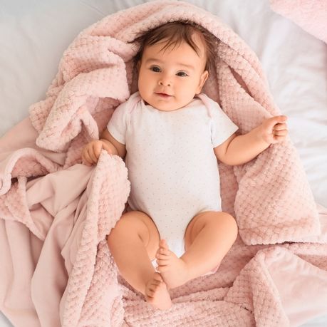 bebe allonge sur un lit sur le dos sur une couverture rose