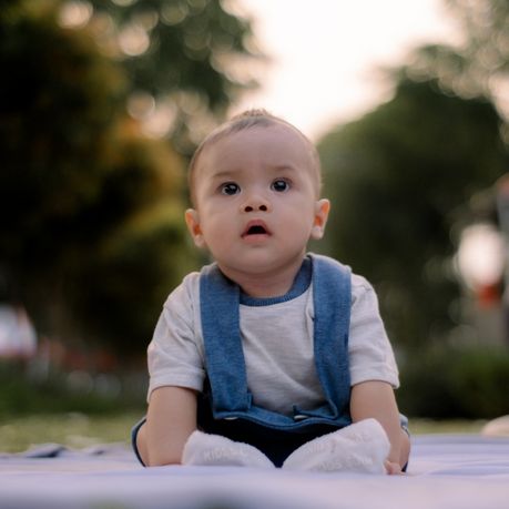 bebe assit dehors avec des arbres flous derriere lui