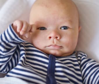 bébé yeux bleu en pyjama blanc et bleu allongé dans son lit