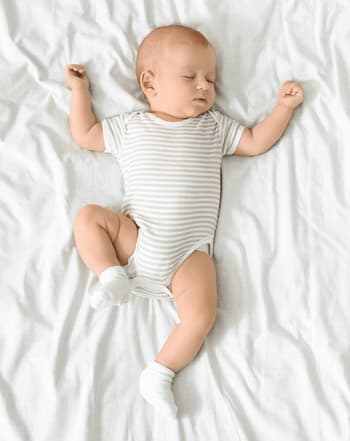 bebe sui dort en body sur un lit blanc