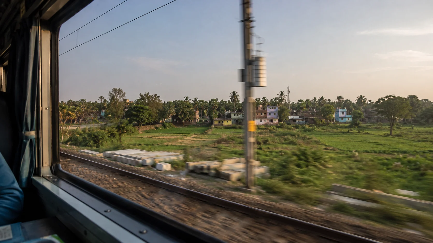 View from a train window — landscape rushing past, the specific feeling of moving through India