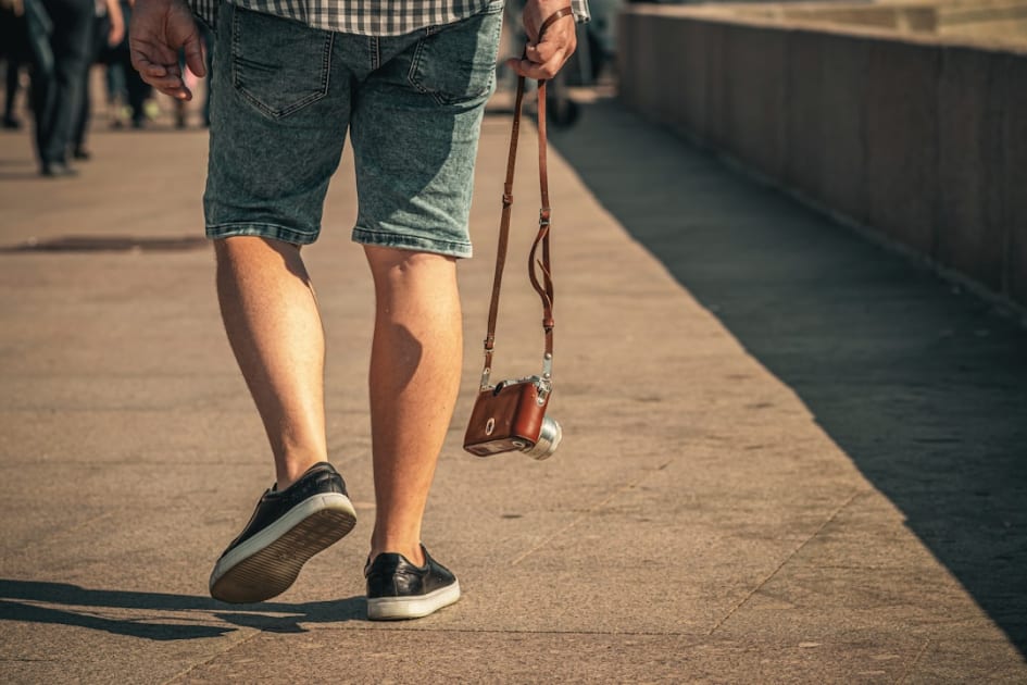a man walking down a sidewalk holding a brown purse