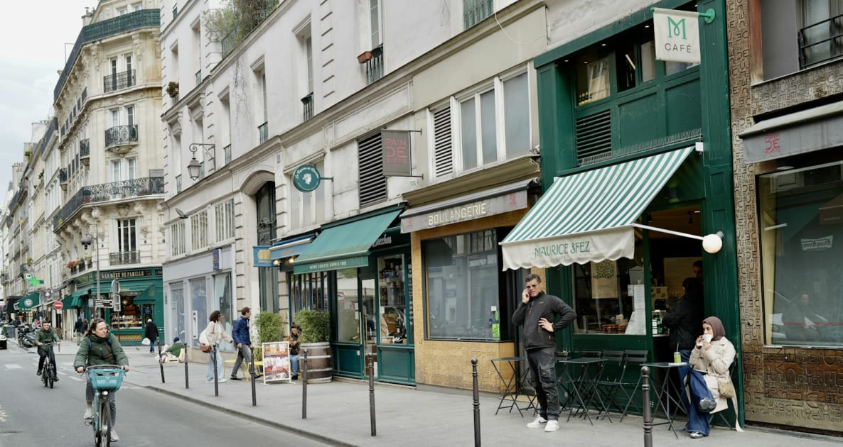 People walk and cycle on a parisian street with shops