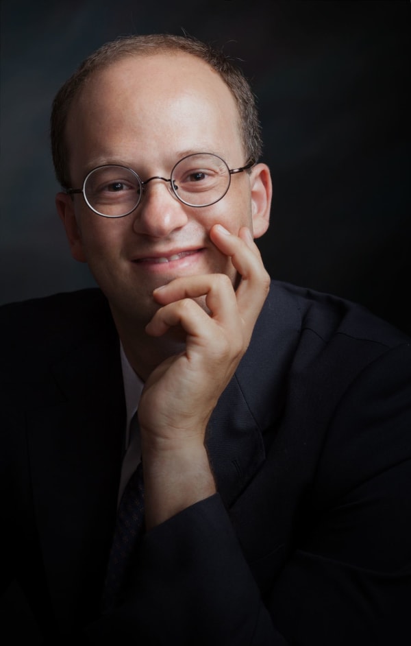 Ritratto in studio di Daniele Camiz con occhiali tondi e mano appoggiata al viso.