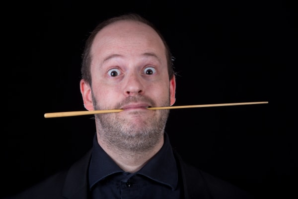 Ritratto ironico di Daniele Camiz con bacchetta orizzontale in bocca e occhi spalancati.